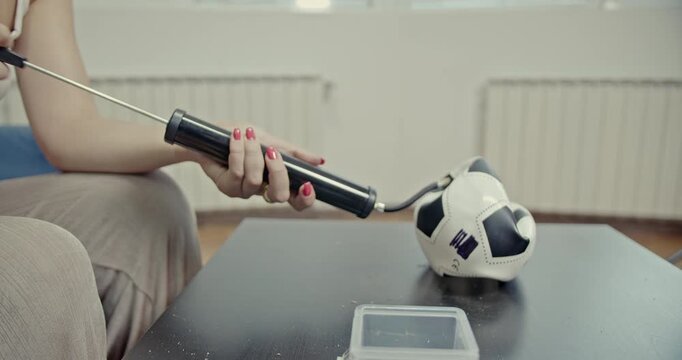 A person skillfully inflates a deflated soccer ball using a hand pump. The ball slowly regains its shape, and the video features clear, audible sounds of the pumping action and air filling the ball.