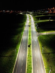 Aerial night view of illuminated highway with green medians and distant city lights &mdash; concept of urban mobility, infrastructure and safe transportation