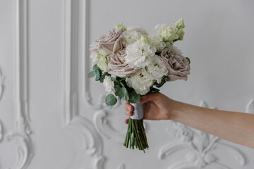 A hand holds a beautiful mixed floral bouquet of taupe roses and white lisianthus (eustoma) against...