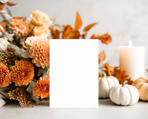 Blank greeting card mockup surrounded by warm-toned autumn flowers, mini white pumpkins, and a burning candle - ideal for seasonal or event stationery