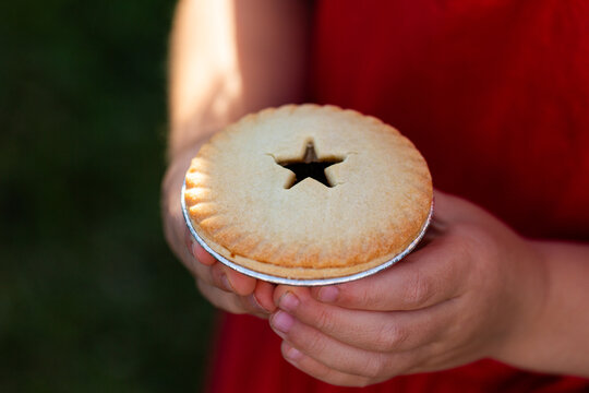 Star shape on fruit mince pie food held in little girls hands at Christmas time outdoors 