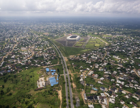 Aerial view of a stadium surrounded by a vast parking area and green spaces blending into the city's edge, Akwa Ibom, Uyo, Nigeria.
