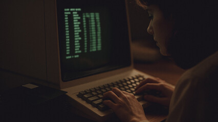 A person intently engaged in coding or hacking activity on a vintage computer, the dim setting enhances the suspense, the glowing green screen illuminating the scene.