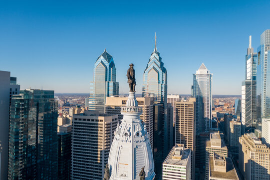 Aerial view of the iconic statue of William Penn atop Philadelphia City Hall, standing tall amidst the modern skyscrapers under a clear blue sky, Philadelphia, Pennsylvania, United States.