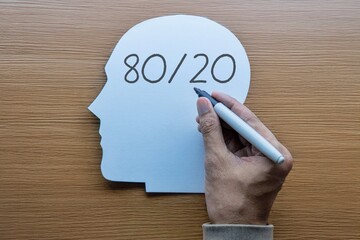 A hand writes the 80 20 rule on a paper cutout of a human head. Pareto Principle, strategy, productivity, and focus concept.