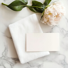 A white towel and a white card with a blank space on it are placed on a marble countertop. The towel is folded neatly and the card is placed on top of it. Concept of cleanliness and organization
