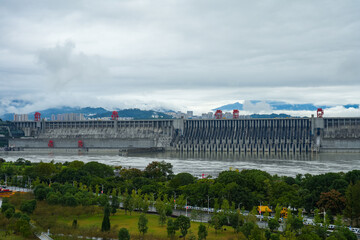 Three Gorges Dam, Yichang City.A vast dam holds back a wide river under a cloudy sky with distant mountains.