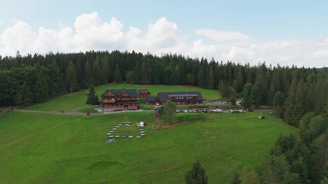 Aerial view of wooden buildings and a parking lot surrounded by lush green grass and dense trees, Jablunkov, Moravian-Silesian Region, Czechia.