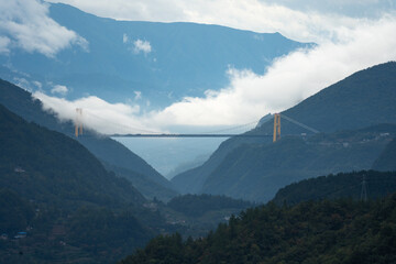 Yellow bridge spans a misty mountain valley at Yichang City, China, connecting steep green slopes...