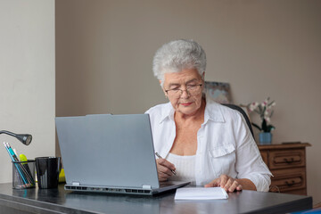 Active senior woman working remotely on laptop from home. Elderly freelancer staying productive in retirement, typing and managing projects online. online banking, insurance, savings, pension