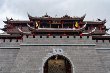 Ancient city gate with layered roofs and red lanterns stands tall in Enshi, China under a cloudy...