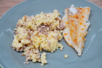 Plate of cooked couscous served with a seasoned fish fillet on a light blue dish.