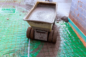 Concrete mixer wheeled wheelbarrow cart stands on green mat, ready to pour fresh cement for floor work