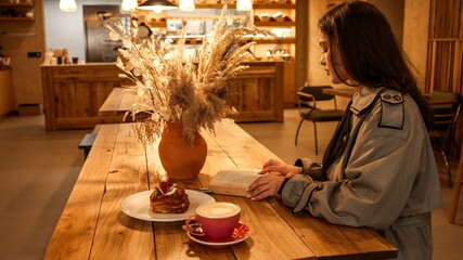 Girl in a stylish coat reading a book in a cozy cafe setting