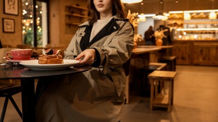 Girl in a trench coat enjoying a pastry and coffee at a cafe.