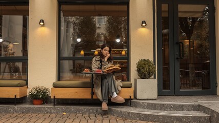 Obraz premium Girl in a trench coat reading a book at a cafe