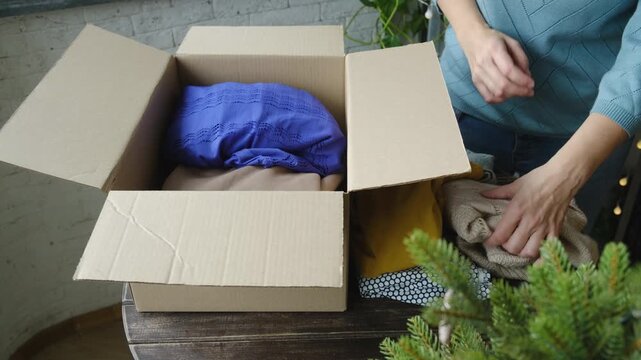Christmas donation, charity concept. Woman packing clothes in donation box.