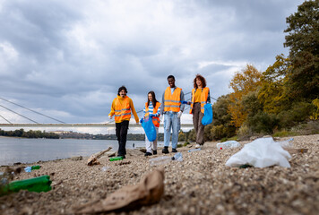 Fototapeta premium Group of volunteers collecting plastic trash on river bank.