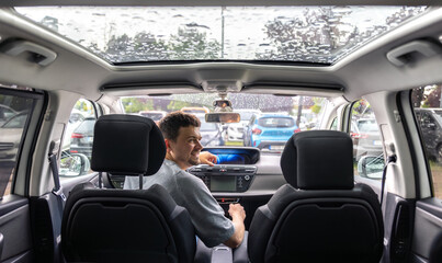 Man in car with panoramic roof on rainy day. Smiling driver inside vehicle. © puhimec