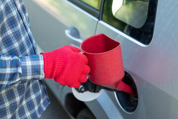 A man is pouring gasoline into the car tank. A man in red gloves stuck a red funnel into the tank of a gray car to pour gasoline into the car's tank