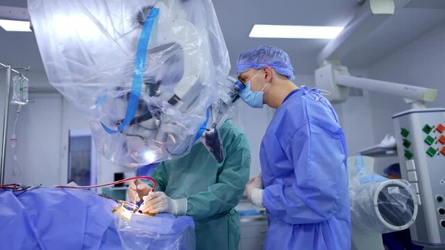 Two neurosurgeons use modern microscope at the operation. Unrecognized chief doctor applies surgical tools at neurosurgery.