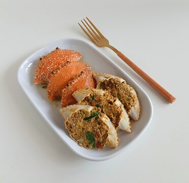 A close-up view of stuffed crab shells filled with a flavorful spiced crab mixture, garnished with herbs and chili, served in a white bowl with a black rim on a clean white background.