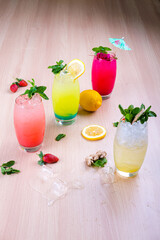 our colorful summer cocktails with mint, lemon, and strawberries on a wood table with melted ice. Perfect for tropical, refreshment, or party drink themes