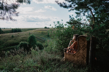 Obraz premium A girl sitting in a chair outdoors, a chair in the forest, a girl sitting in a chair in the forest, a sofa outdoors, a sofa in the forest, furniture in the forest, a girl relaxing, an unusual vacation