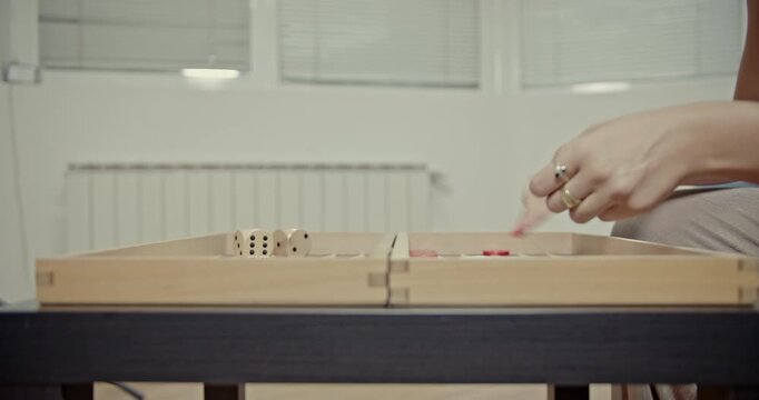 Enjoy the authentic sounds of backgammon as hands skillfully shake dice and move checkers across the wooden board. A close-up captures the classic board game in action.