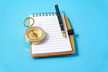 A fountain pen and a brass compass resting on notebook.