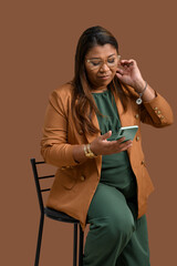 Focused woman in brown blazer using smartphone on brown background