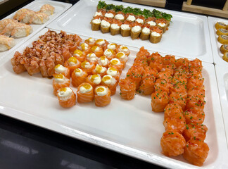 Trays of fresh Japanese sushi, at an Asian buffet restaurant. Salmon rolls, prawn sashimi, and fish roe.