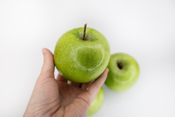 Hand holding apple with scattered green apples flat lay on white background with copy space