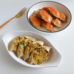 A close-up view of stuffed crab shells filled with a flavorful spiced crab mixture, garnished with herbs and chili, served in a white bowl with a black rim on a clean white background.