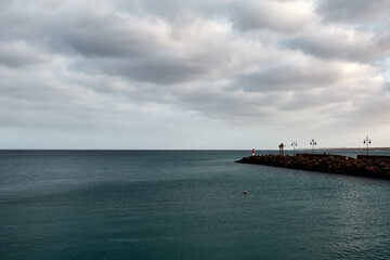 Fototapeta premium A calm sea under a cloudy sky with a rocky pier extending into the water, perfect as a peaceful nature wallpaper.