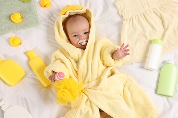 Cute baby in bathrobe, clothes and bathroom accessories on bed, top view