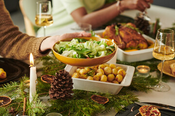 Caucasian adult hand serving green salad at Christmas holiday table with roasted chicken, potatoes,...