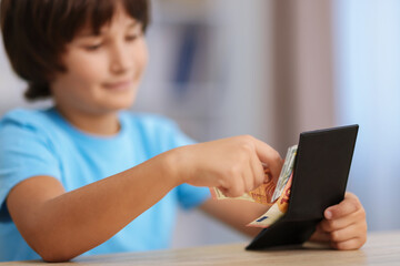 Fototapeta premium Boy with pocket money at wooden table indoors, selective focus