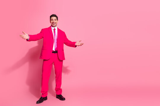 Funky young man in pink suit posing charismatically in modern studio against bright background