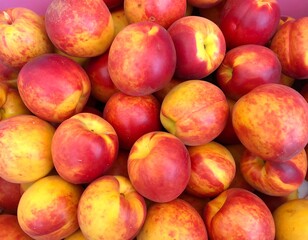 A close-up shot displays a pile of vibrant stone fruits, predominantly yellow and red, highlighting their smooth skin and juicy flesh
