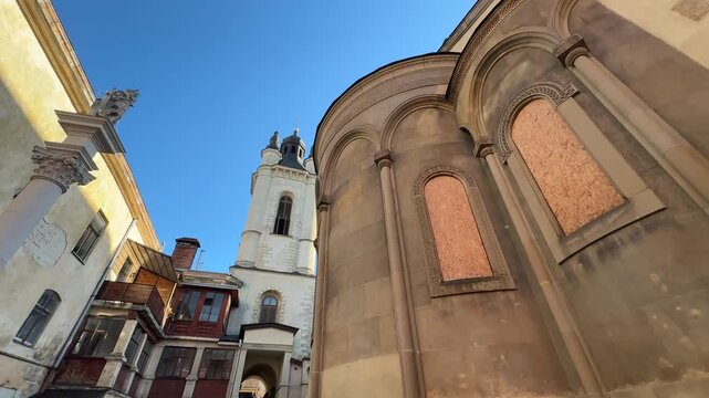 An artistic low-angle view in a Lviv courtyard shows the church apse and historic tower, with red wooden balconies and a blue sky overhead, highlighting the old architecture