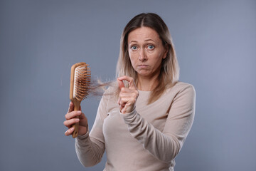 Alopecia problem. Worried woman taking her lost hair from brush on grey background
