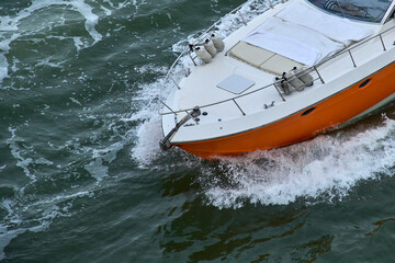 Obraz premium The bow of an orange luxury yacht cutting through the water with spray