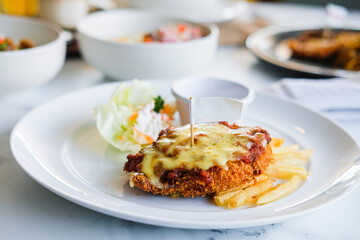 A serving of crispy chicken parmigiana or schnitzel topped with melted cheese, served with french fries and a salad on a white plate