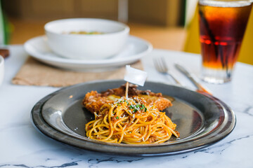 
A fusion meal featuring crispy chicken schnitzel with gravy and a side of spaghetti bolognese, served on a dark plate on a marble table in a restaurant