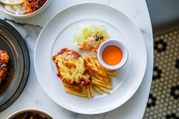 Gourmet Chicken Parmigiana served with crispy French fries, fresh salad, and a side of dipping sauce on a white plate