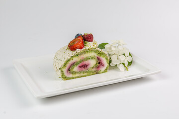 Pistachio meringue roll with berry cream and fresh fruits on a white plate.