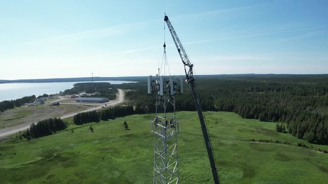 Aerial View of Men Working at the Top of the Telephone Tower on a Sunny Day in the Village of Port-menier, Anticosti Island, Quebec, Canada 