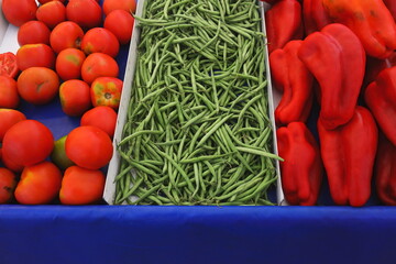 Fresh vegetables at market — red tomatoes, green beans, and red bell peppers arranged in colorful rows. Concept of healthy eating, vegan diet, organic agriculture, and natural nutrition.
