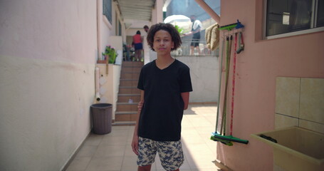 Hispanic teenage Latin boy of African descent standing casually in suburban alleyway, showing calm...